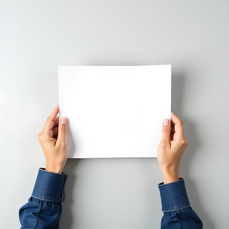 Woman holding blank paper sheet on grey background, top view. Mockup for designの素材