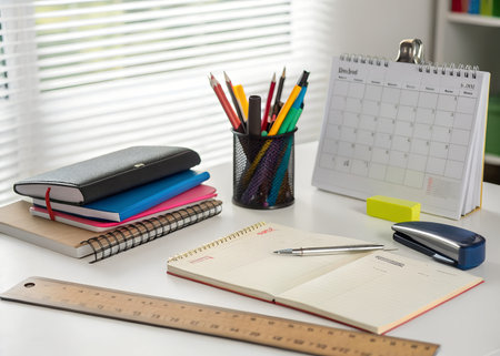 A desk with school supplies including a stack of notebooks, pencils in a holder, a ruler, and a calendar on a white backgroundの素材