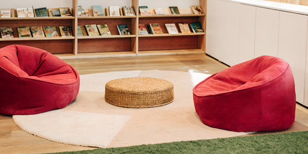 Cozy reading corner with two plush red beanbag chairs and a round textured ottoman on a soft rug in a room with bookshelvesの素材