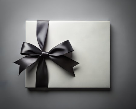 Elegant white gift box with a black satin ribbon and bow, presented on a dark gray background, symbolizing luxury and special occasionsの素材