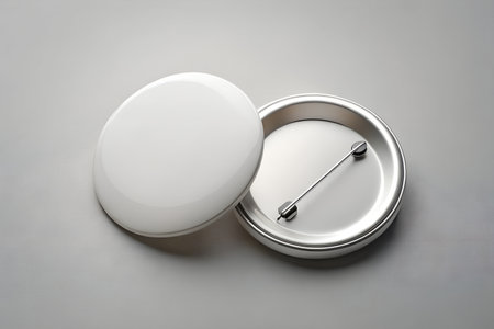Two blank white round badges, one closed and one open showing the metal backing and pin, isolated on a neutral gray background, ready for customizationの素材