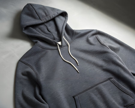 Closeup shot of a dark grey hooded sweatshirt with a front pocket and white drawstrings, showcasing its texture and stitching detail on a neutral backgroundの素材