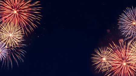 Bright red and gold fireworks exploding in the dark night sky, creating a festive celebration background display with copy space.の素材