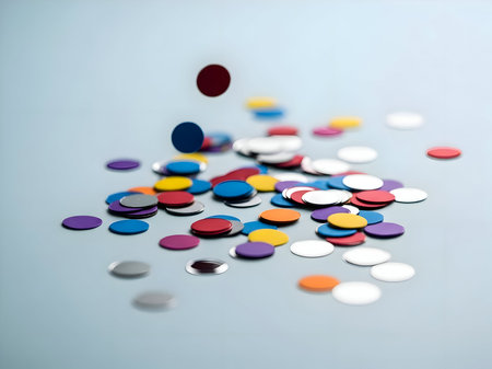 Vibrant circular confetti pieces in various colors scattered and falling on a light blue surface, creating a festive background for celebrationsの素材