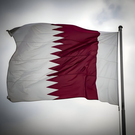 The national flag of qatar, a distinctive maroon and white serrated design, flutters proudly against a cloudy sky.の素材