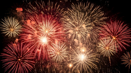 Vibrant red and gold fireworks explode across the night sky, illuminating the darkness with spectacular bursts of light, celebrating a festive occasion.の素材