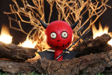 Halloween Devil Doll on black background with dead trees and fire.