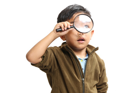 Asian boy using a magnifying glass on a white background.の写真素材