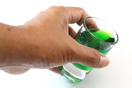 Man hand holding a glass measuring cup with a green liquid isolate on white background.の写真素材