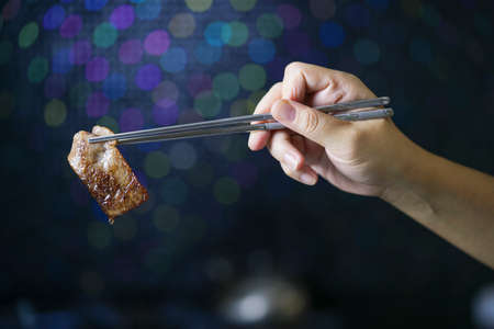 Hand using chopsticks to pick up wagyu beef, Grilled wagyu beef over black background.の写真素材