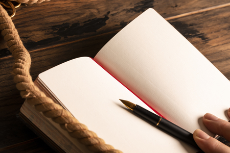 Man holds his hand on antique notebook. Blank sheet for writing text. Marine rope and pen.の写真素材
