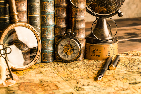 Antique clock on the background of vintage books. Mechanical clockwork on a chain. Fountain pen and glasses.の写真素材