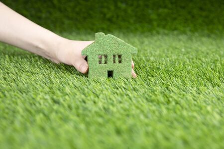 A man holds in his hand a small eco house. A miniature copy of a house on the grass.の写真素材