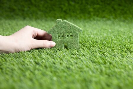 A man holds in his hand a small eco house. A miniature copy of a house on the grass.の写真素材