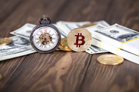 The cryptocurrency Bitcoin coin. Gold coin. Vintage pocket watch stand on the background of bundles of money. Roman numerals on the dial.の写真素材