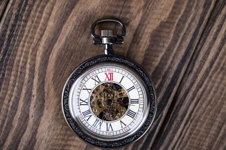 Vintage pocket watch on a chain lie on a wooden table. Roman numerals on the dial.の写真素材