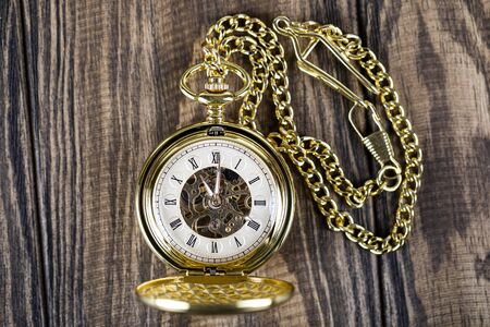 Vintage pocket watch on a chain lie on a wooden table. Roman numerals on the dial.の写真素材