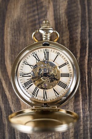 Vintage pocket watch on a chain lie on a wooden table. Roman numerals on the dial.の写真素材
