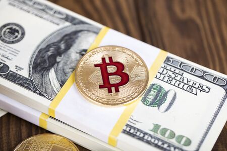 The cryptocurrency Bitcoin coin. Gold coin. Gold coin lies on a bundle of hundred-dollar bills.の写真素材