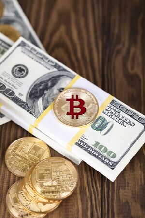 The cryptocurrency Bitcoin coin. Gold coin. Gold coin lies on a bundle of hundred-dollar bills.の写真素材