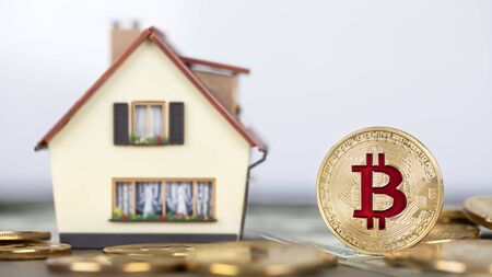 The cryptocurrency Bitcoin coin. Gold coins and packs of hundred dollar bills. A miniature copy of the house.の写真素材