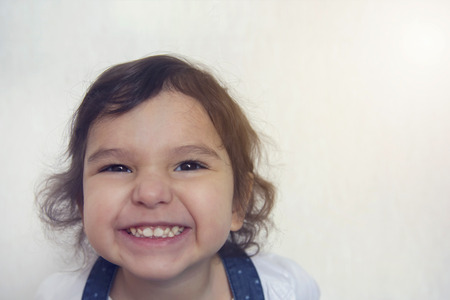 Little curly naughty little girl smiling, against a white wall backgroundの写真素材