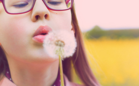 Girl and dandelion, on a rapeseed field, yellow blurred backgroundの写真素材
