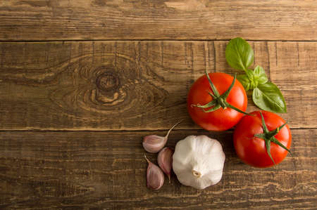 Vegetables on a wooden table, tomatoes and garlic head with a green basil, Vegetables perfectly harmoniously laid out on a wooden background.の写真素材
