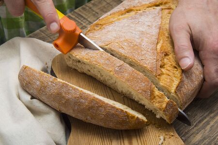 Man's hands cutting bread on the wooden plank.の写真素材