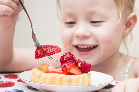 Little girl eating a strawberry tart outdoorsの写真素材