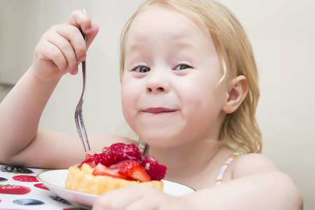 Little girl eating a strawberry tart outdoorsの写真素材