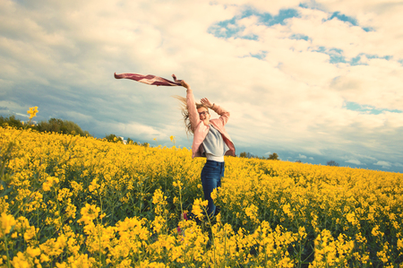 happy independent girl in rapeseed field in windy weather waving a waving scarfの写真素材