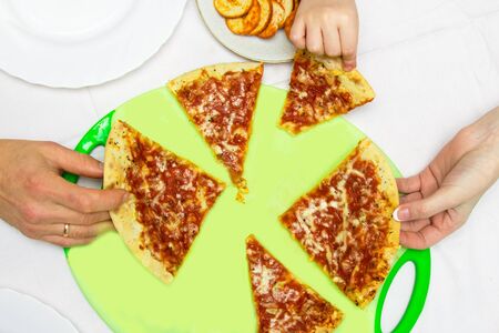 family at the round table is eating pizza, taking slices of pizza straight from the cutting hopperの写真素材
