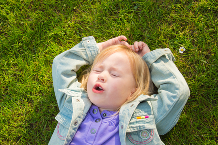 little funny girl singing lying on green grass on the streetの写真素材