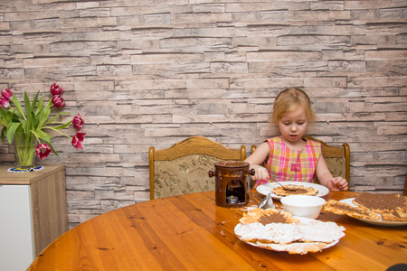 a five-year-old girl smears Belgian waffles at a table with chocolateの写真素材