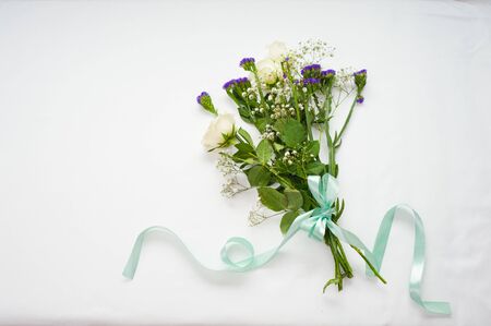 womens hands are preparing a gift bouquet with white roses. tying it with a blue satin ribbon. gift concept for a woman. Concept work of the flower girl.の写真素材