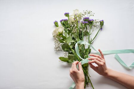 women's hands are preparing a gift bouquet with white roses. tying it with a blue satin ribbon. gift concept for a woman.の写真素材