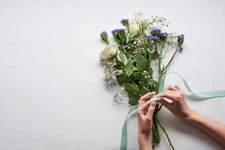 women's hands are preparing a gift bouquet with white roses. tying it with a blue satin ribbon. gift concept for a woman.の写真素材