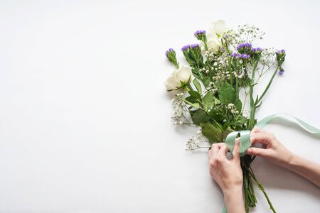 women's hands are preparing a gift bouquet with white roses. tying it with a blue satin ribbon. gift concept for a woman.の写真素材