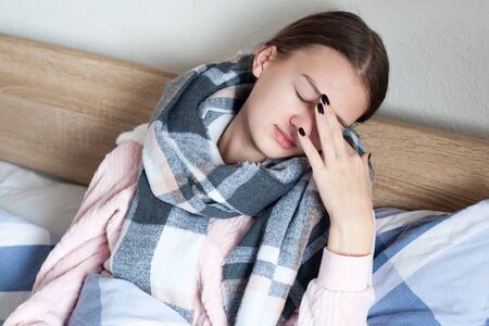 student is lying at home in bed with flu symptoms. A girl in kravat with a scarf around her neck. Headache and malaiseの写真素材