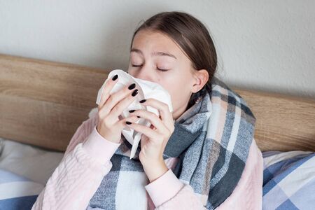 A sick girl with a headache sits under a blanket. Sick woman with seasonal infections, flu,...