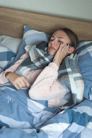 A girl suffers from pain in the temples. A girl of a student lies at home in bed with flu symptoms.の写真素材