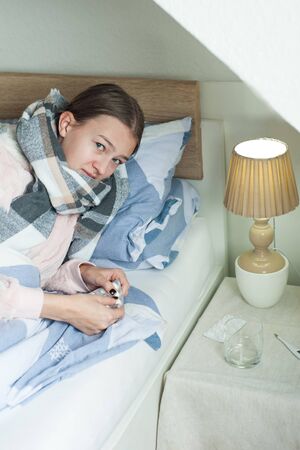Student is lying at home in bed with flu symptoms. girl takes medicineの写真素材