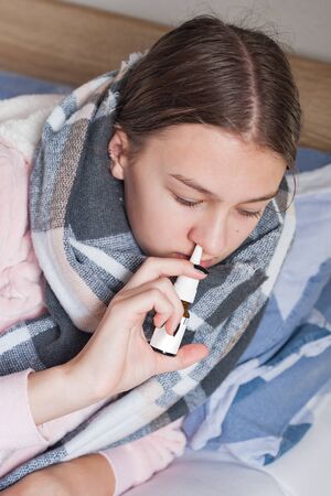 Female student girl is lying at home in bed with flu symptoms. girl uses a nose sprayの写真素材