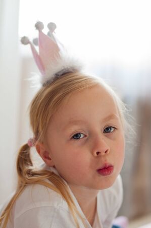 Girl with a crown on her head cute poses for the camera at home in daylightの写真素材