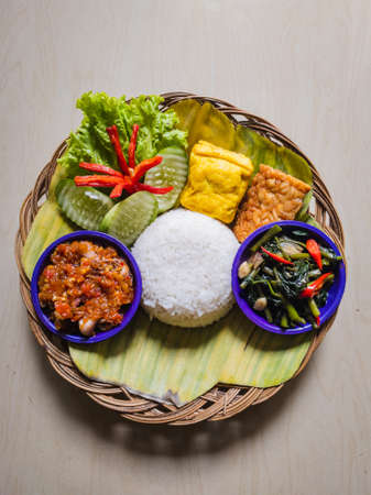 Indonesian Traditional Food From Sundanese Nasi Liwet with various kinds of side dishes such as Tofu or tahu, tempe, Cah kangkung, squid sauce (sambal cumi) and vegetables cucumber and lettuce.の写真素材