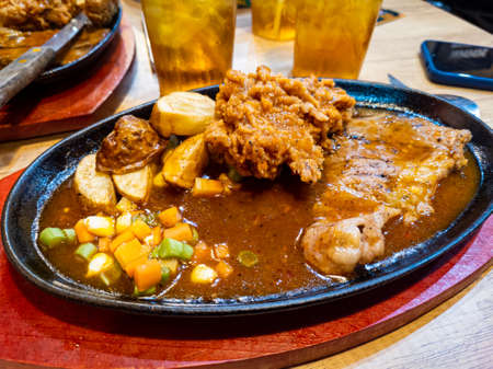 Close up thin grilled sirloin beef steak on a hot plate with fried chicken, potato, vegetables and black pepper sauce at indonesian restaurant.の写真素材