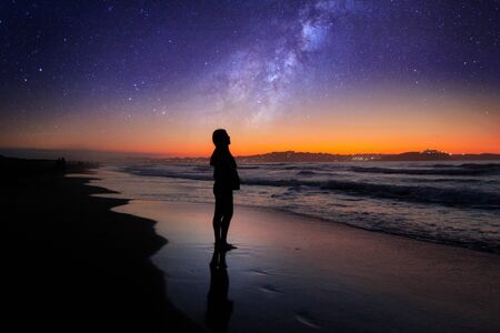 Girl on the beach with the sunset and the galaxy in the sky.