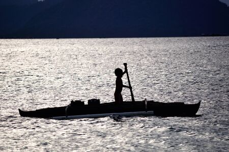 Silhouette of a young boy paddling a boat in Celebes sea Sabah Borneo Malaysiaの写真素材