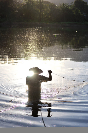Silhouette if a fisherman and fishing net in the waterの写真素材